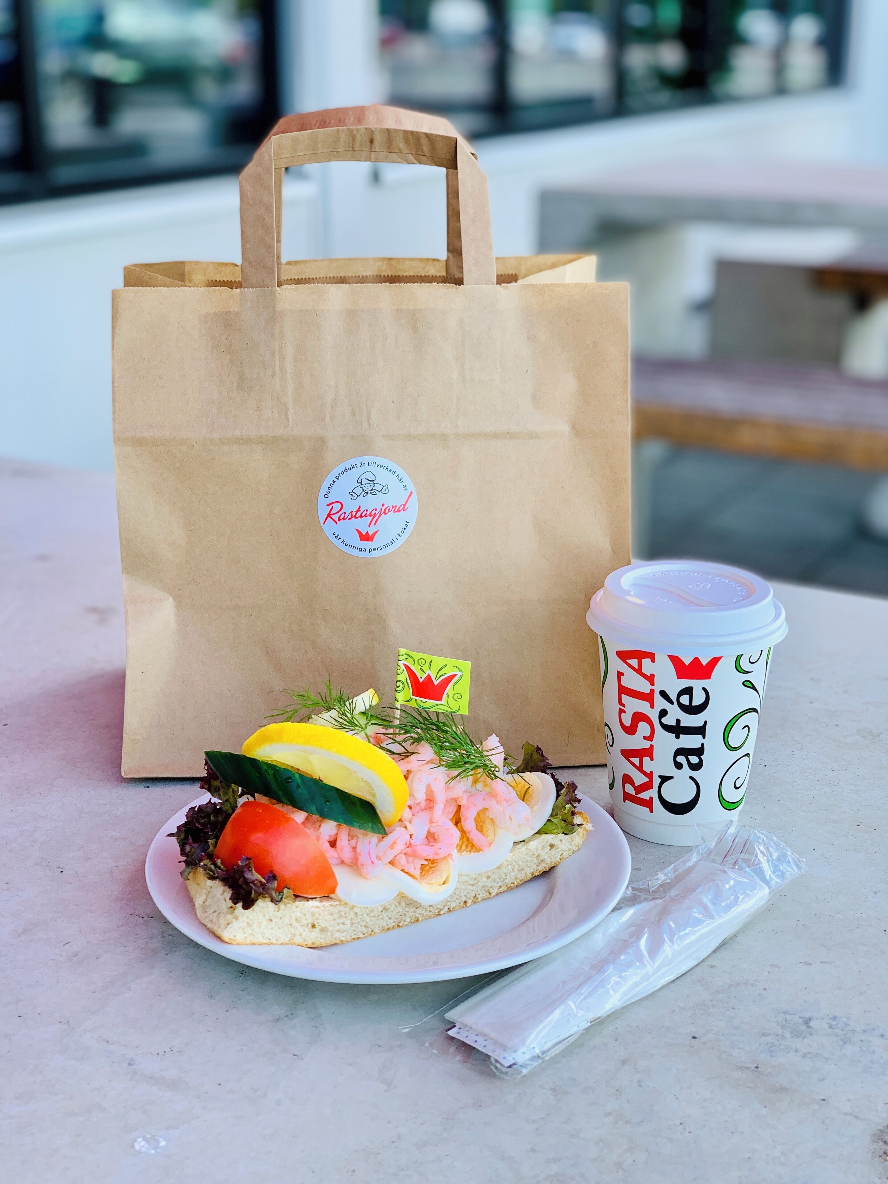 A sandwich on a plate, a paper bag, and a cup labeled "Rasta Café".