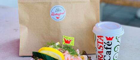 A sandwich on a plate, a paper bag, and a cup labeled "Rasta Café".