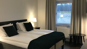 Quarto de hotel com uma cama, mesas de cabeceira, abajur, janela com cortinas e vista para o exterior.