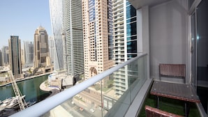 A balcony with a glass railing overlooking a cityscape, a small table, and a wicker chair. - Piks Key - Marina Torch Tower (Dubai)