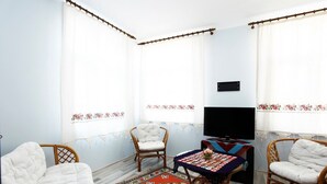 Una habitación con dos sillas de mimbre, una mesita con un tapete colorido, un televisor de pantalla plana y un adorno en la pared.