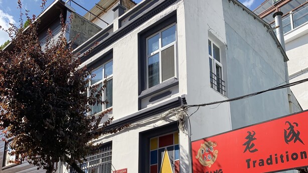 Un restaurante chino tradicional con un letrero rojo, una colorida decoración en la ventana y fachada de ladrillo.