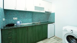 Una cocina con gabinetes verdes, microondas, cafetera y lavadora.