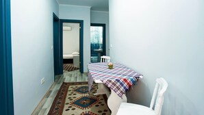 Un pasillo estrecho con una mesa de comedor cubierta por un mantel a cuadros, una alfombra estampada y una silla blanca.