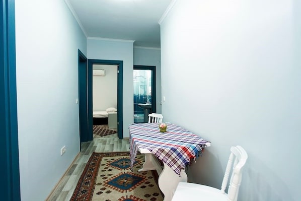 Un pasillo estrecho con una mesa de comedor cubierta por un mantel a cuadros, una alfombra estampada y una silla blanca.