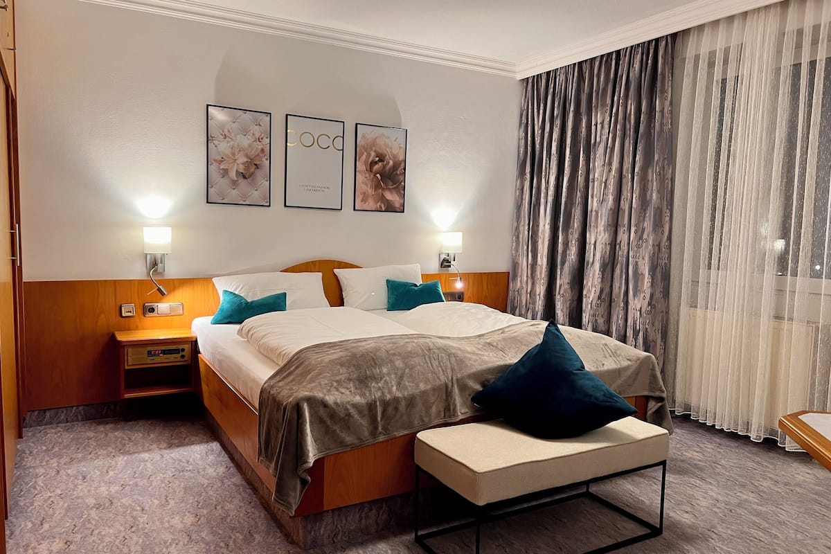 A hotel room with a bed, bedside tables, a nightstand, a lamp, and a window with curtains.