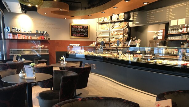Un angolo di panetteria con una vetrina di dolci e una bacheca con il menu.