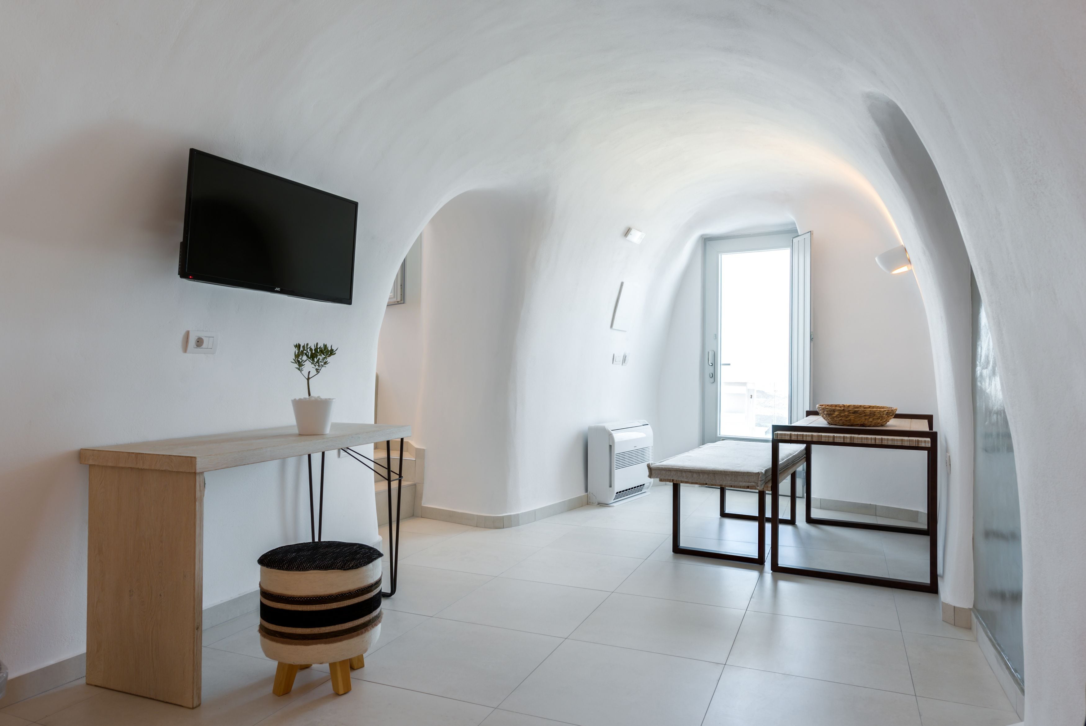 Una cucina moderna e minimalista con schermo piatto, un bancone in legno, un piccolo sgabello e un'area pranzo con tavolo e sedie.