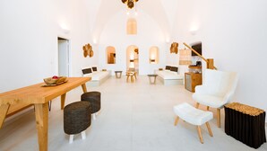 A spacious living area with a wooden dining table, wicker chairs, a white sofa, and a white armchair. - Iriana Suites (Santorini)