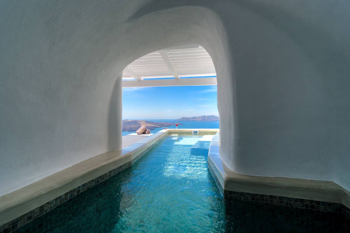 Vista clara de una piscina con fondo de azulejos, rodeada de paredes blancas y un techo con vigas de madera blanca.