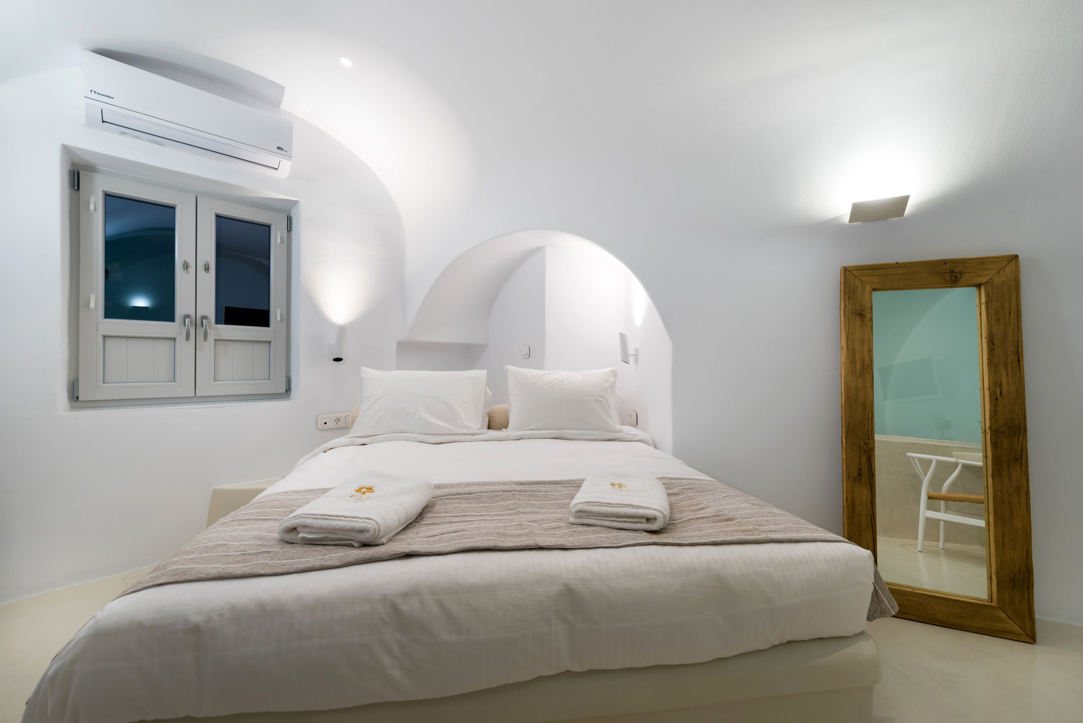 Un dormitorio con cama, ventana, equipo de aire acondicionado y espejo.