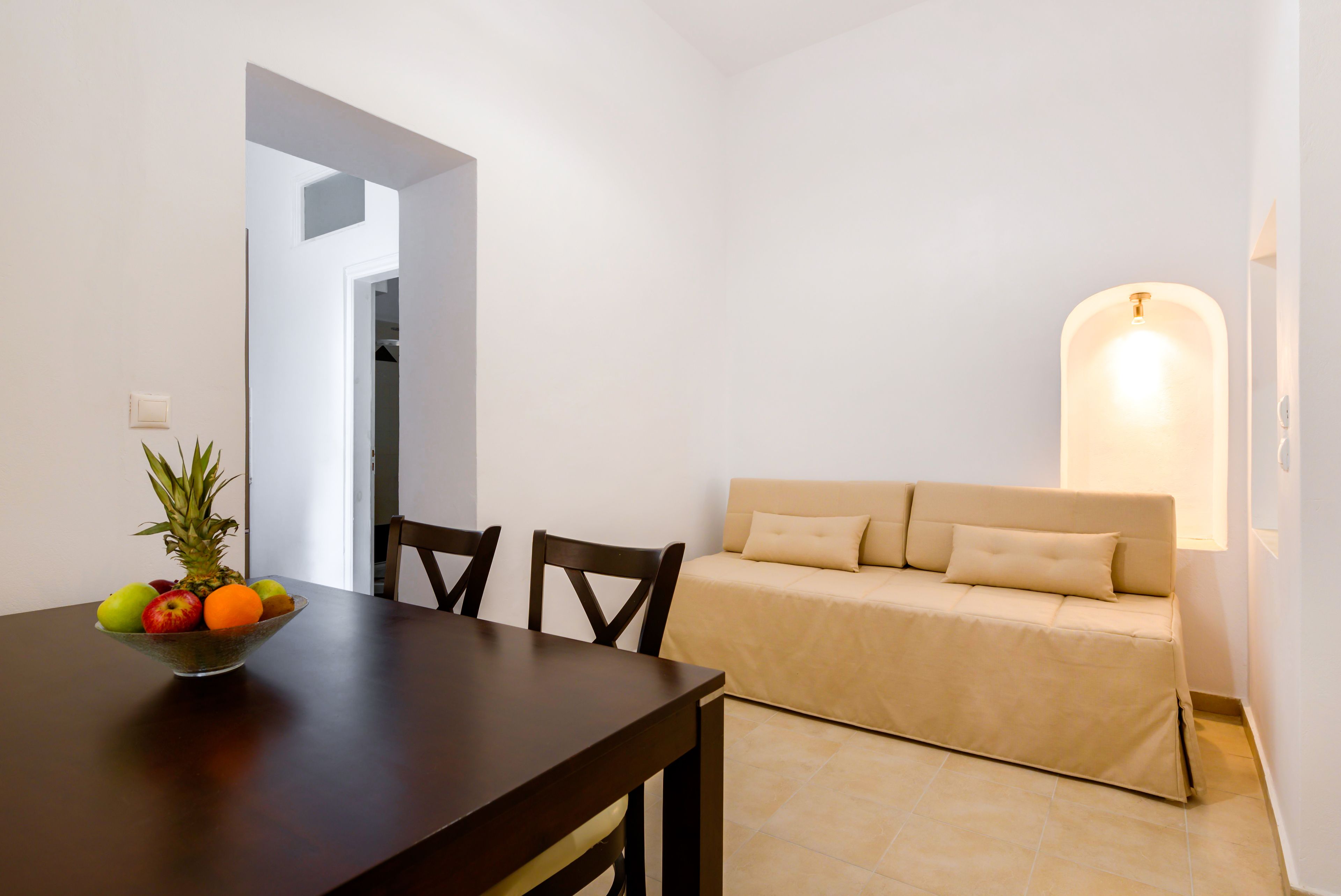 A dining area with a wooden table, a bowl of fruit, and a beige sofa.