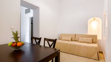 A dining area with a wooden table, a bowl of fruit, and a beige sofa.