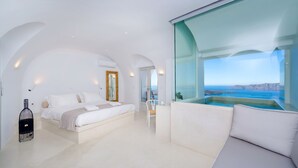 A modern hotel room with a large bed, a sitting area with a view of the sea, and a glass-enclosed jacuzzi. - Iriana Suites (Santorini)