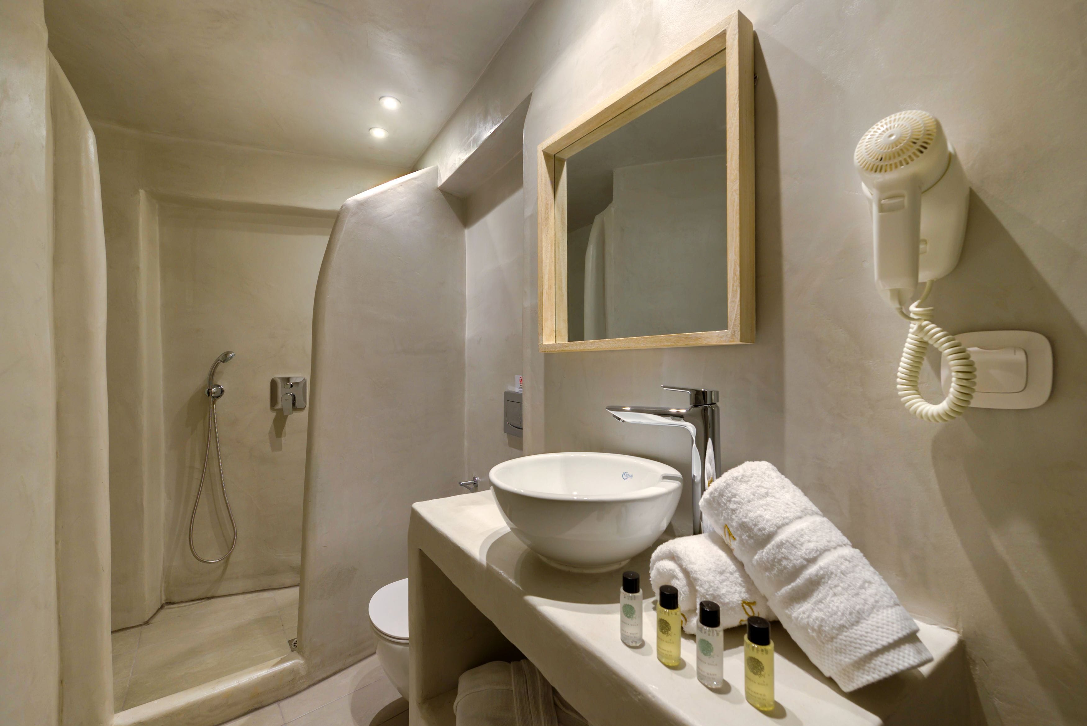 Un baño moderno con un lavamanos grande de color blanco, un espejo, un secador de pelo y una ducha.