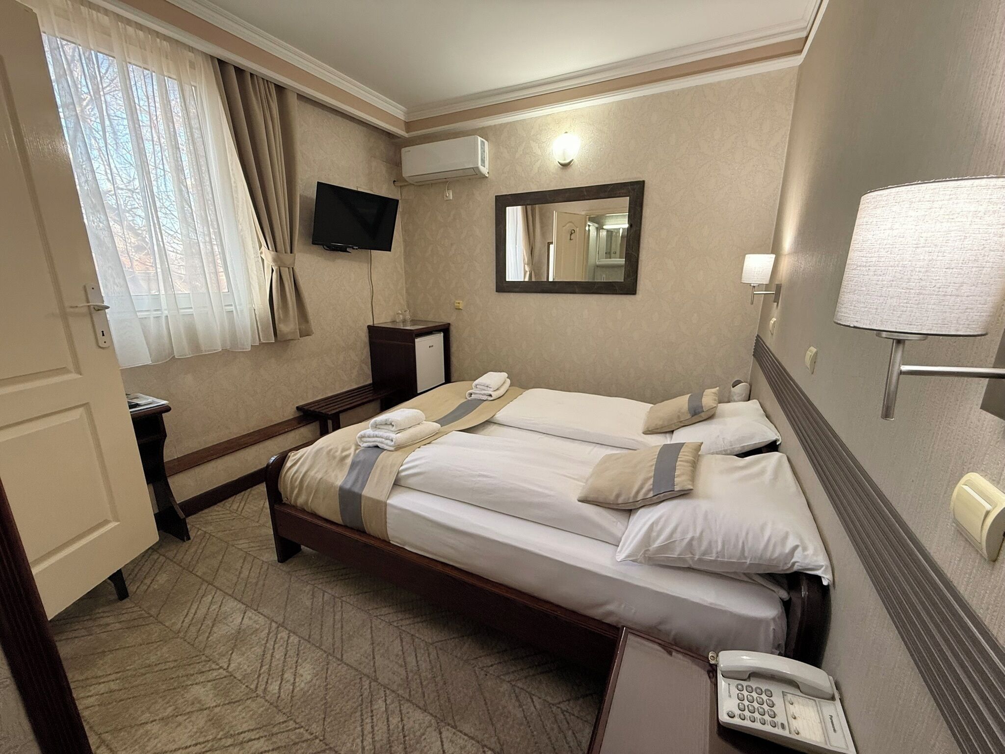 A hotel room with two beds, a television, an air conditioning unit, a telephone, and a mirror.