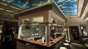 Een barruimte met een plafonddecoratie van wolken, een toonbank met barstoelen en een zichtbaar menubord.
