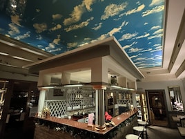 Zona de bar con un mural de nubes en el techo, una barra con taburetes y un menú visible.