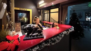 Een receptiebalie met kerstboom en kerstster, een kantoorruimte met een bord, en een trap naar een andere kamer.