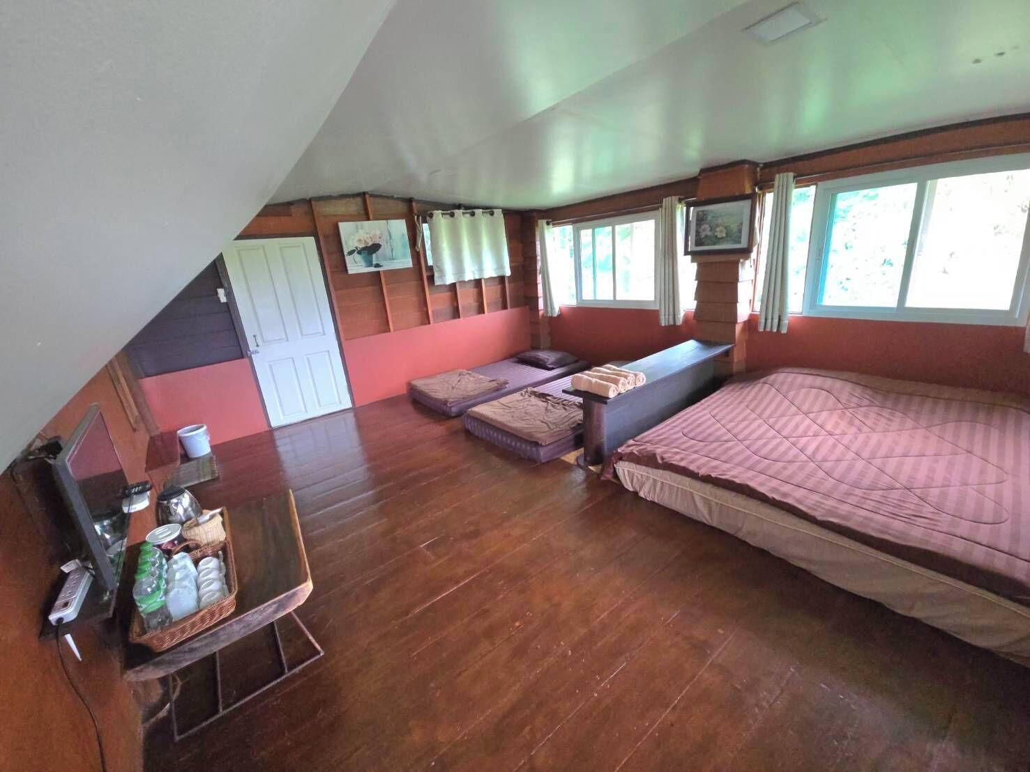 A room with a large bed, a small sofa, a table with a basket of items, and a window with curtains.