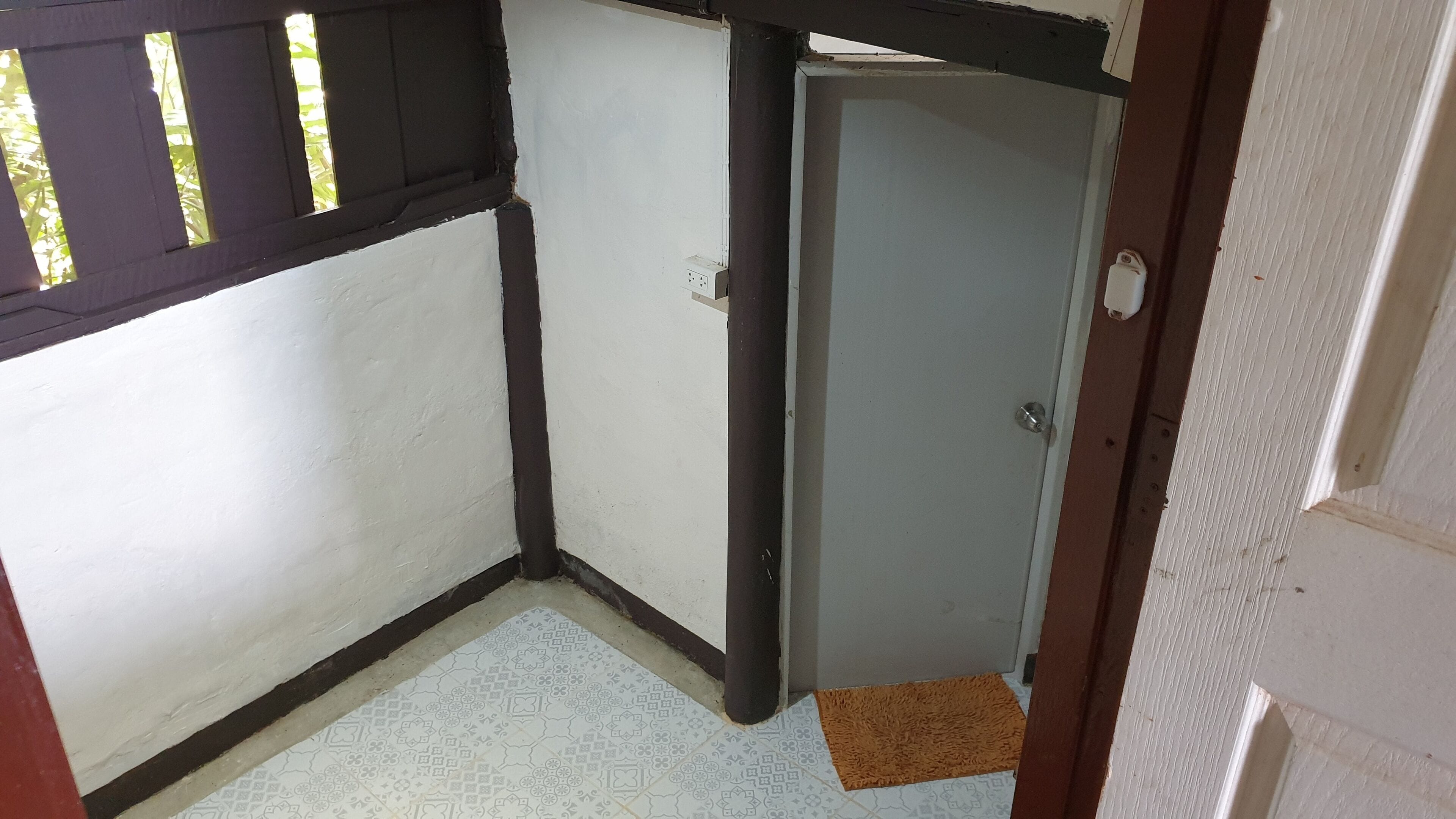 A corner room with a door, a window with bars, and a patterned floor.