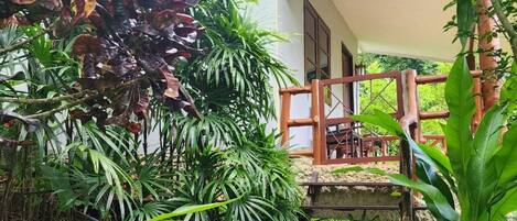 Una escalera de madera que lleva a una casa con tejado de tejas, rodeada de abundante vegetación.