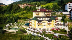 A multi-story hotel with a pool, outdoor seating, and a mountainous backdrop.