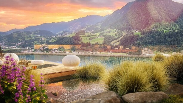 A scenic lakeside view with mountains in the background, a dock with spherical structures, and a small house near the water.