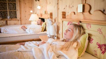 Ein Zimmer mit Holzwänden und einem Bett mit blumigem Kopfteil. Ein Nachttisch mit Lampe und einer Vase steht daneben.