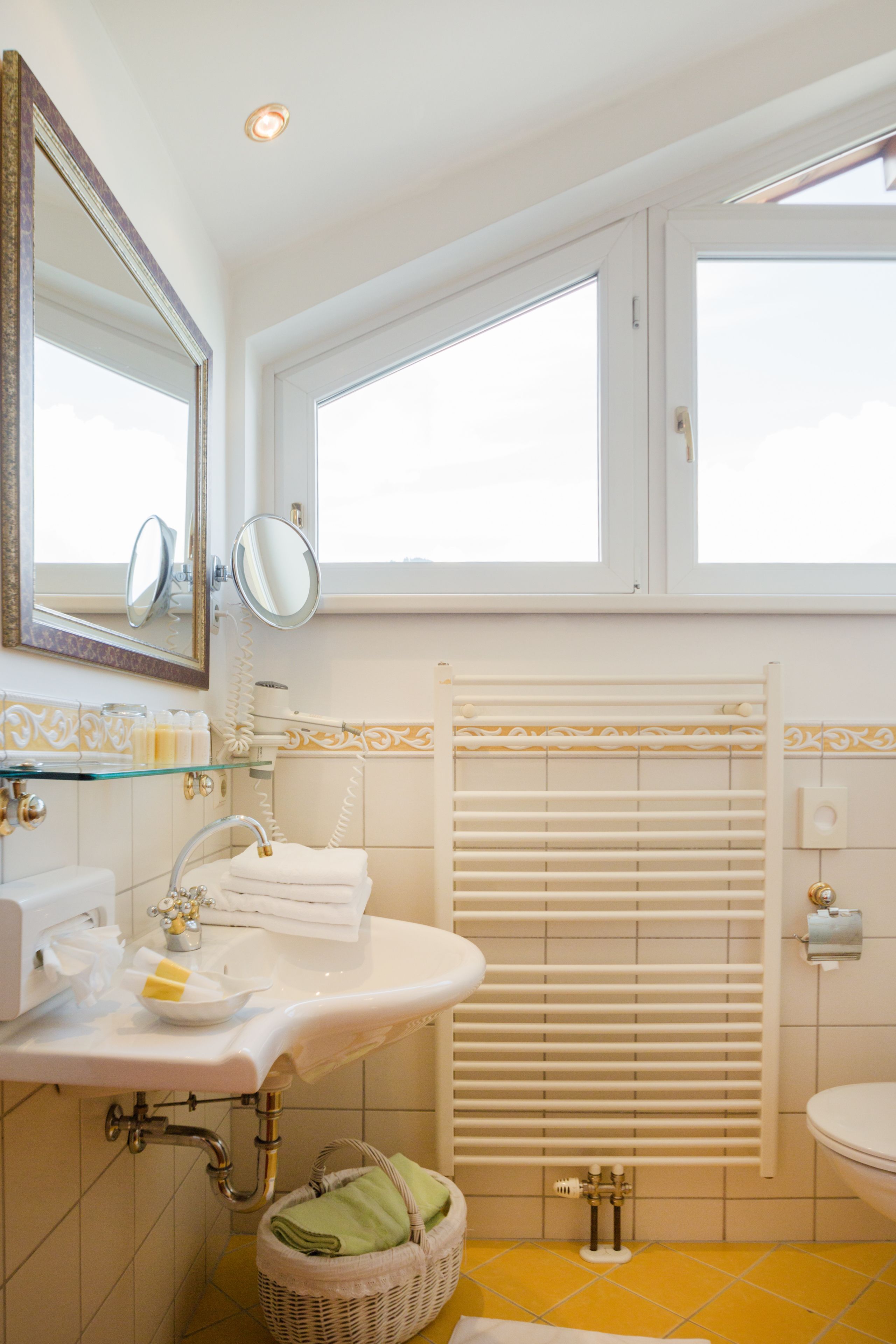 Un baño con lavamanos blanco, espejo, inodoro, estante de vidrio y ventana con persianas.