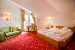 A hotel room with a large bed, a green sofa, a desk, and a window with curtains. - Hotel AlpenSchlössl (Sankt Johann im Pongau)