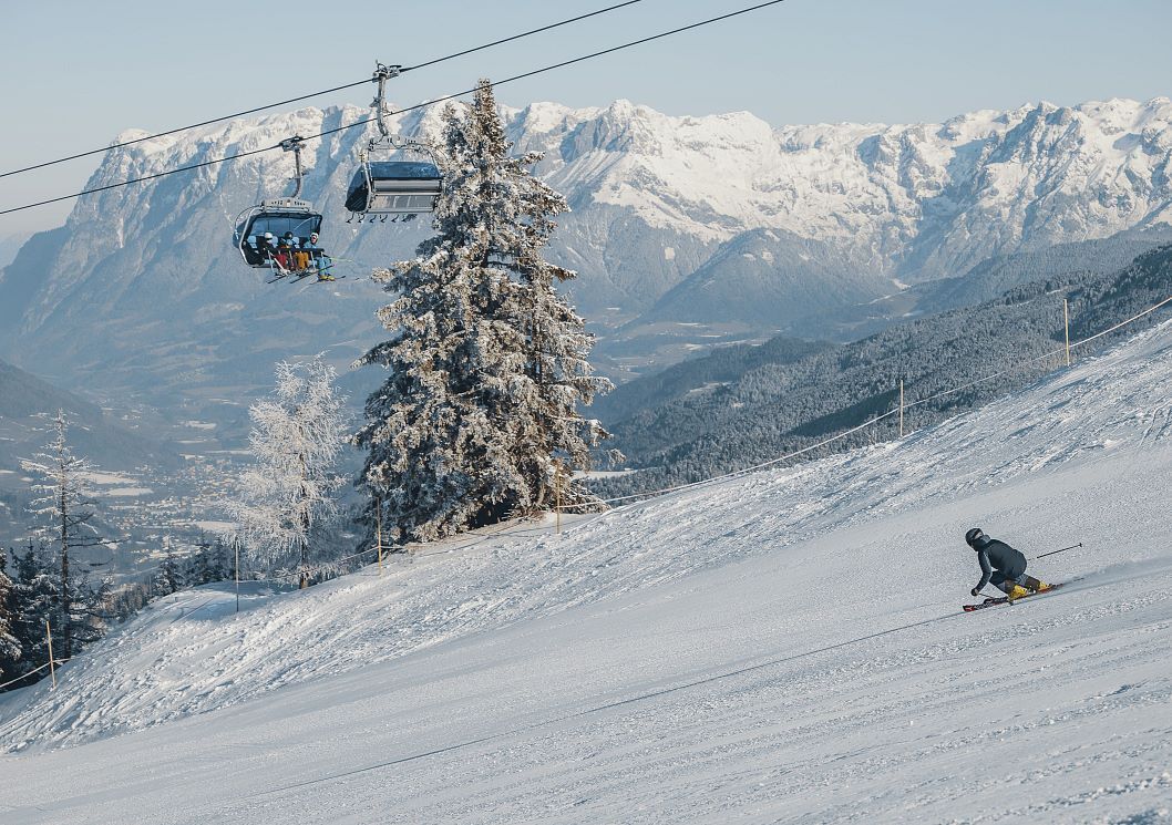 Um teleférico com cadeira, uma árvore coberta de neve e um esquiador em uma encosta.