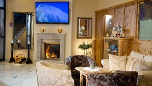 A cozy living room with a fireplace, a television mounted above it, and a wooden cabinet with decorative items.