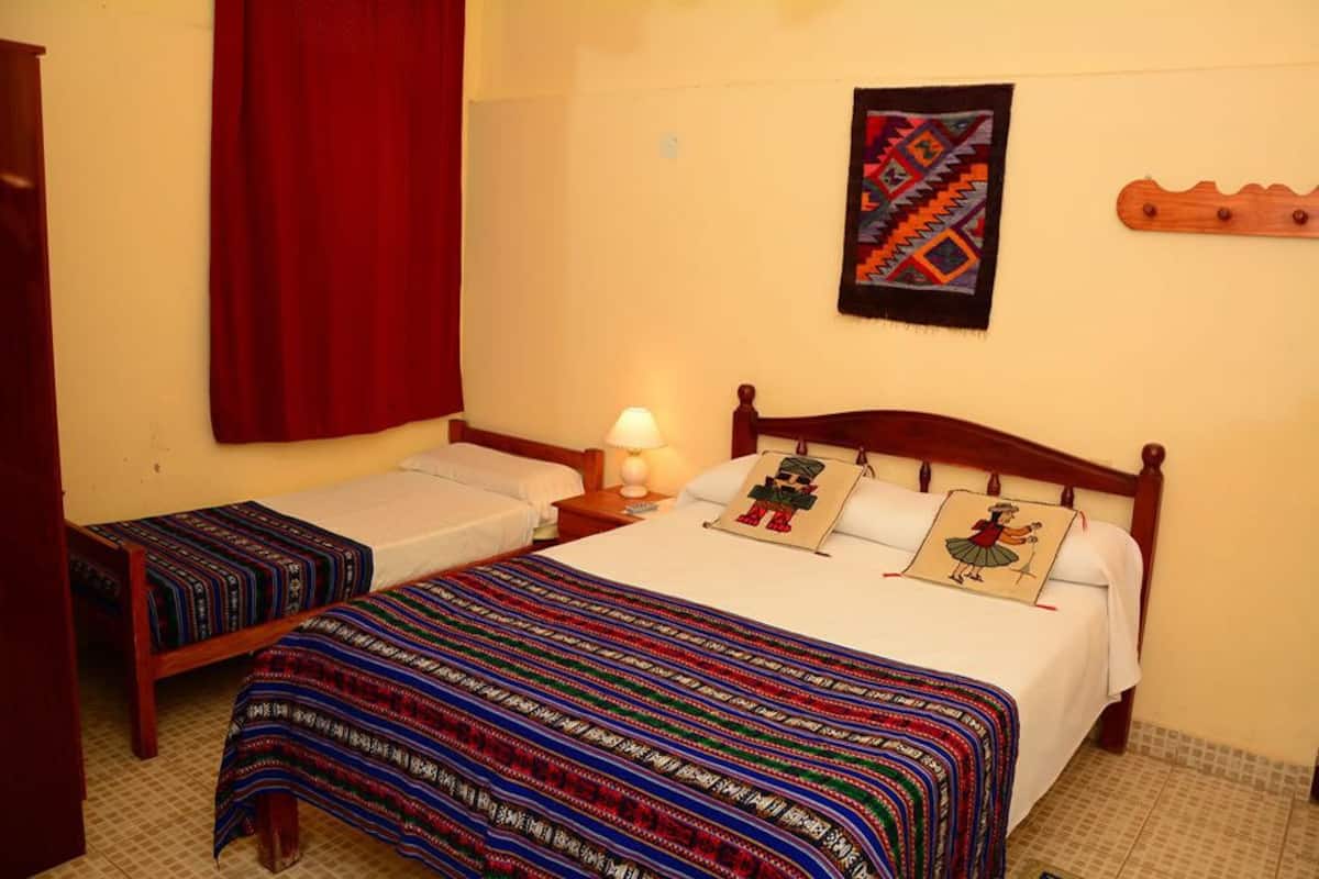 Quarto com duas camas, cortina vermelha, tapeçaria na parede e cabeceira de madeira.