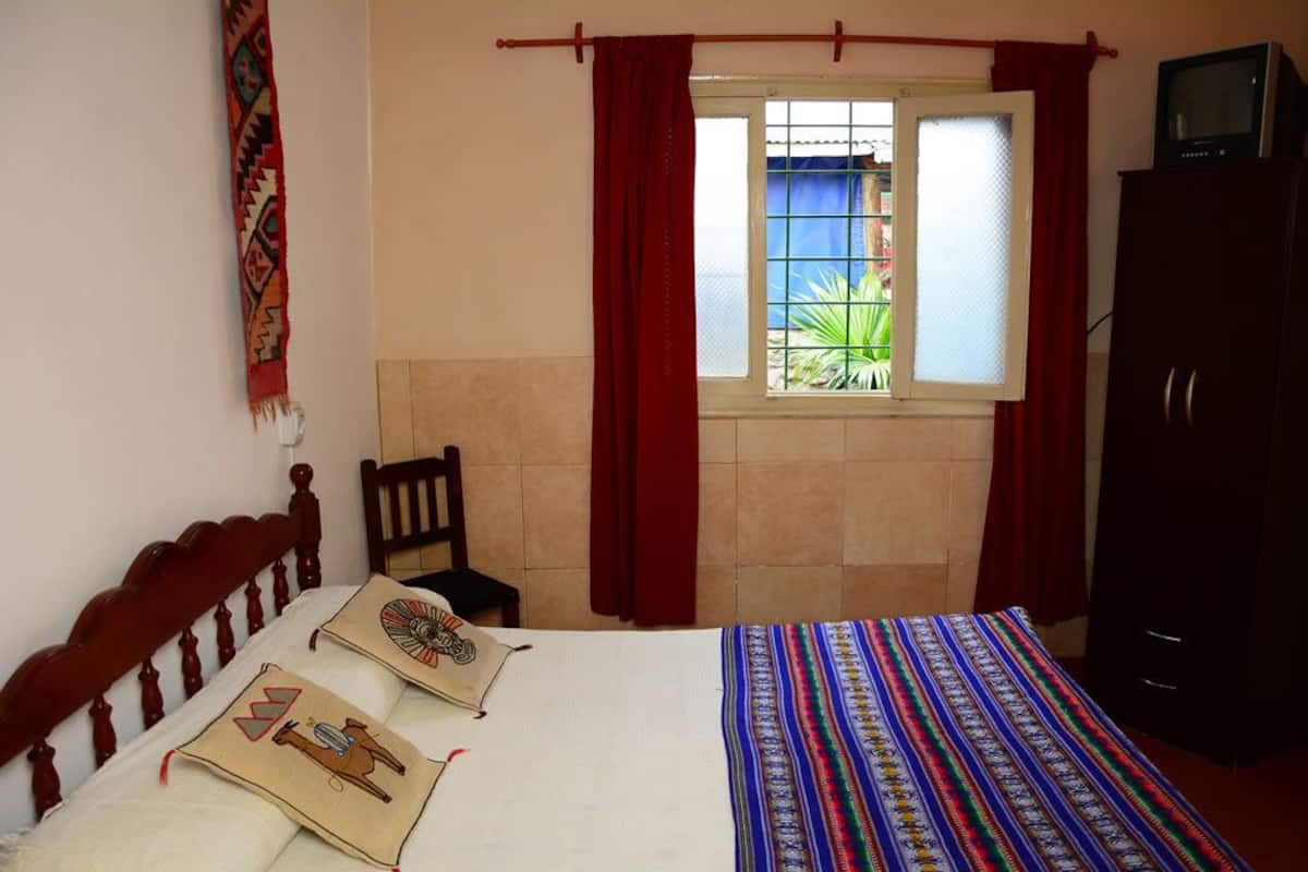 Quarto com cama, cadeira, guarda-roupa e janela com cortinas.