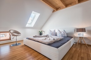 A bedroom with a skylight, a bed with striped pillows, a modern chair, and a bedside table with a lamp.