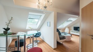A modern loft apartment with a glass dining table, a red ottoman, a chandelier, and a TV in a separate room. - Appartmenthaus am Erlbach (Buch am Erlbach)