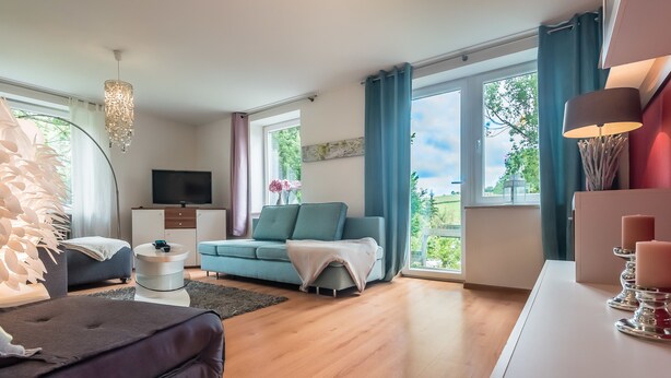 A modern living room with a sofa, a television, and a dining area with candles. - Appartmenthaus am Erlbach (Buch am Erlbach)