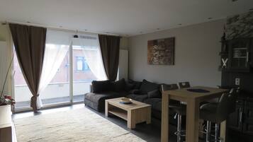 Een moderne woonkamer met een bank, salontafel en een eethoek met stoelen en een tafel.