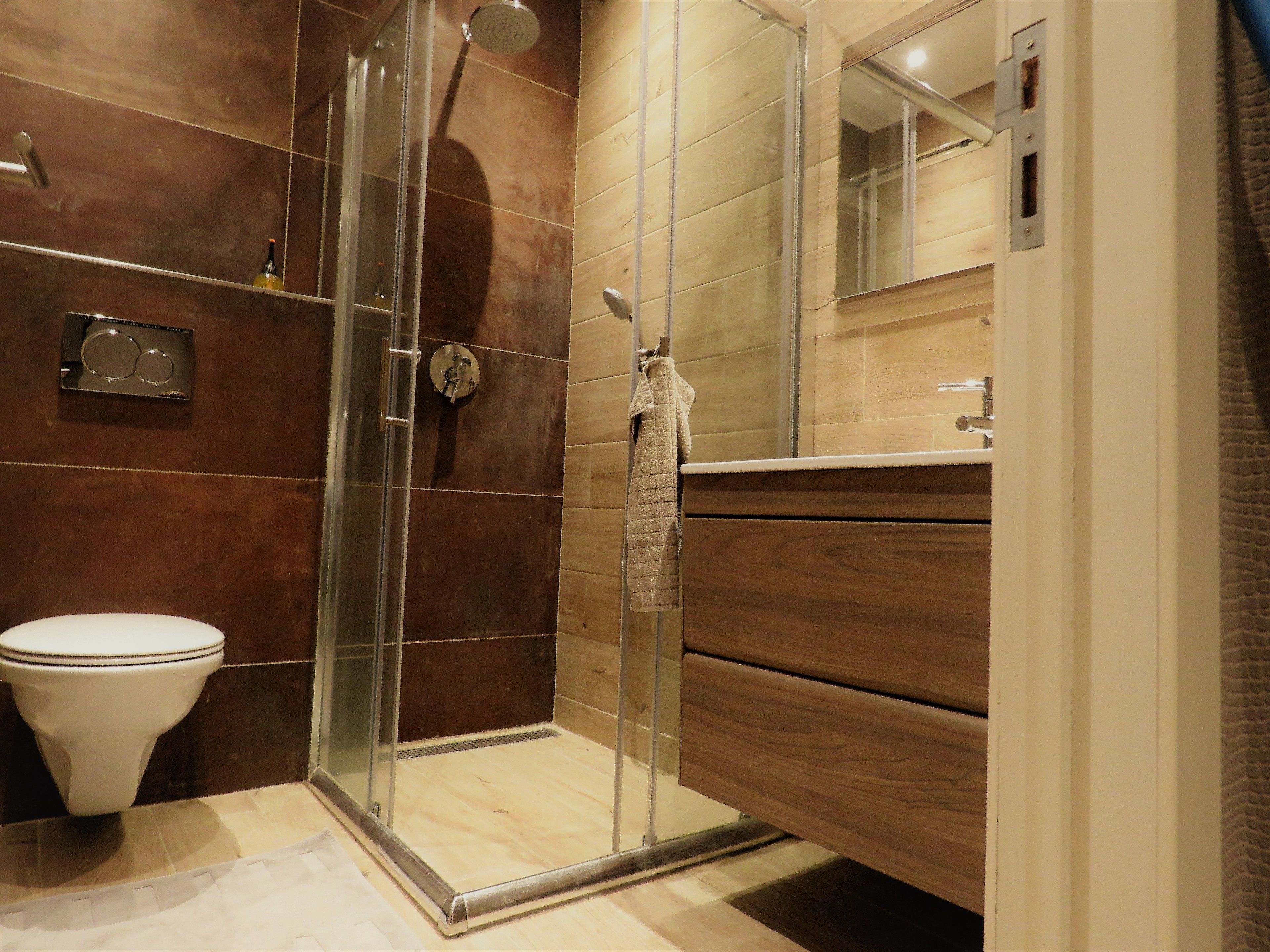 Un baño moderno con ducha de vidrio, inodoro y tocador de madera con espejo.
