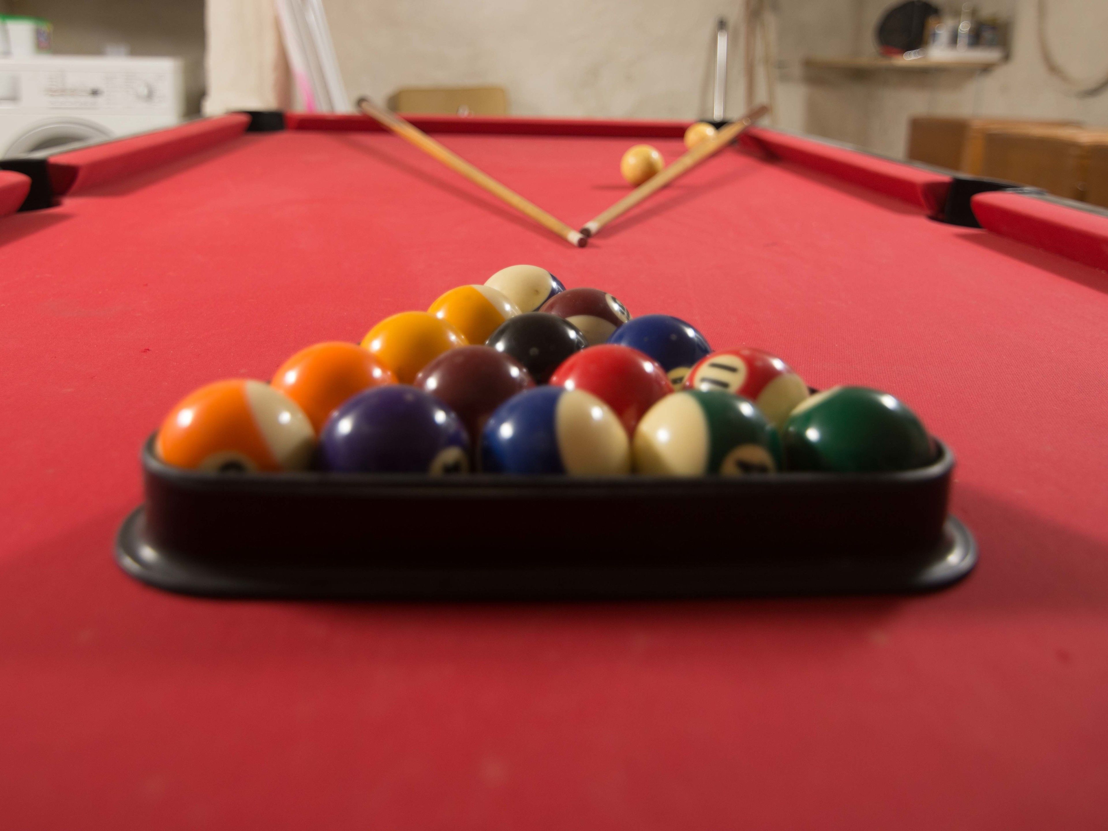 A pool table with a red felt surface and a set of billiard balls arranged in a triangle formation.