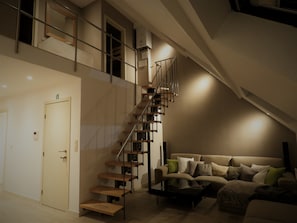 Un intérieur moderne avec un escalier en bois, un canapé agrémenté de coussins et une table basse en verre.