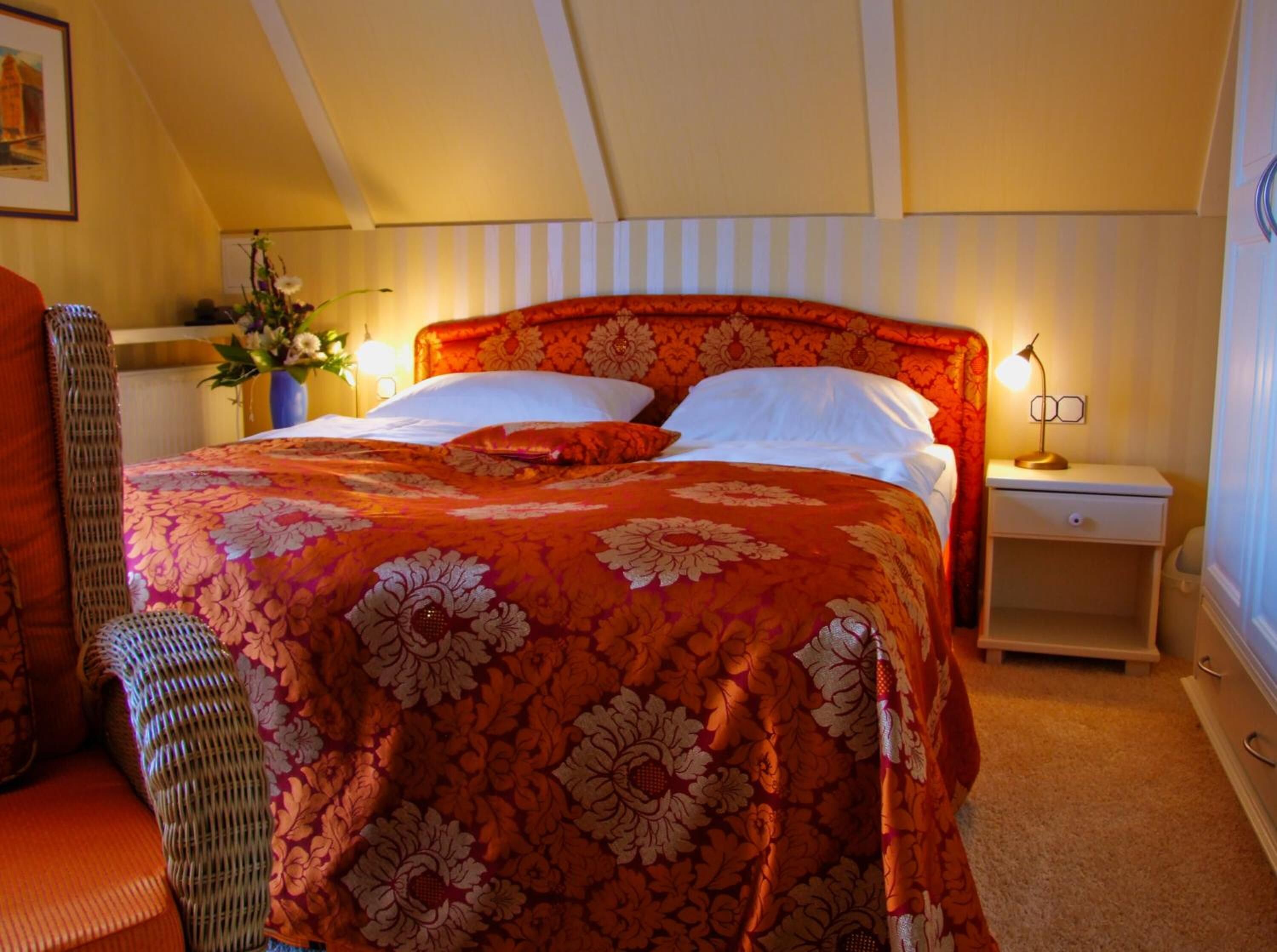 A bedroom with a large bed, a nightstand, a lamp, and a chair.