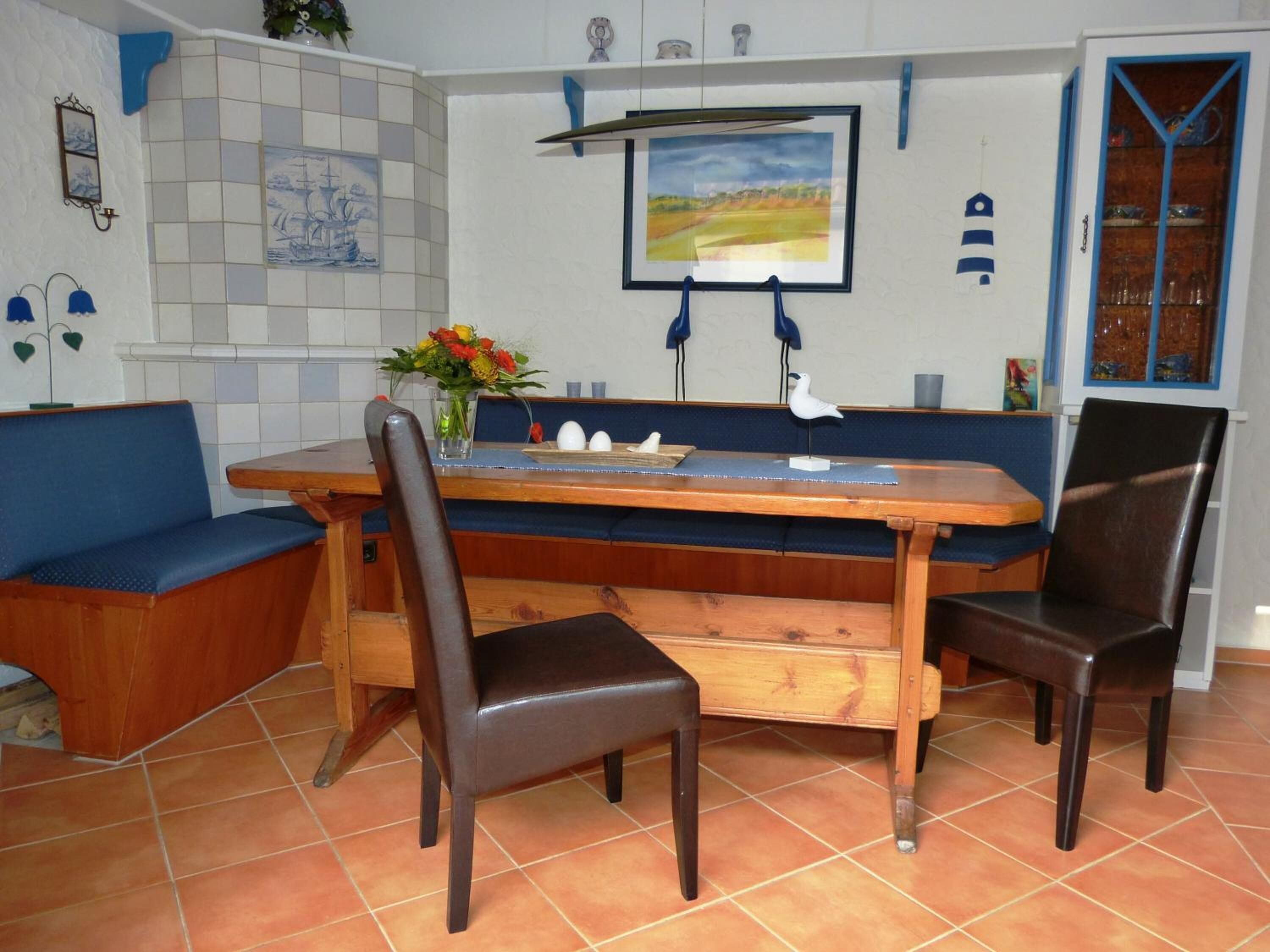 A dining area with a wooden table, two chairs, a bench, and a wall-mounted picture.