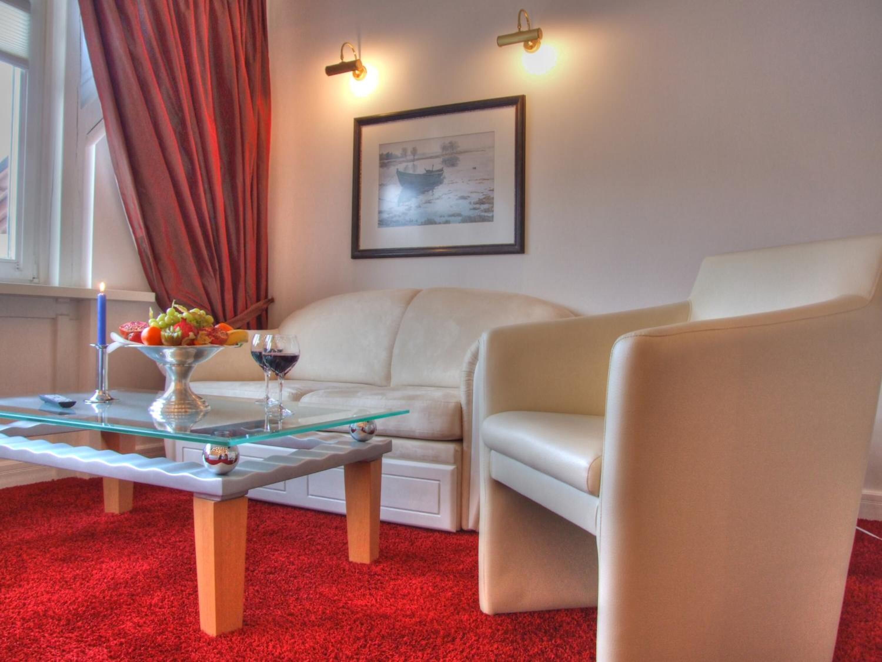 A living room with a glass coffee table, a white sofa, a red carpet, and a framed picture on the wall.