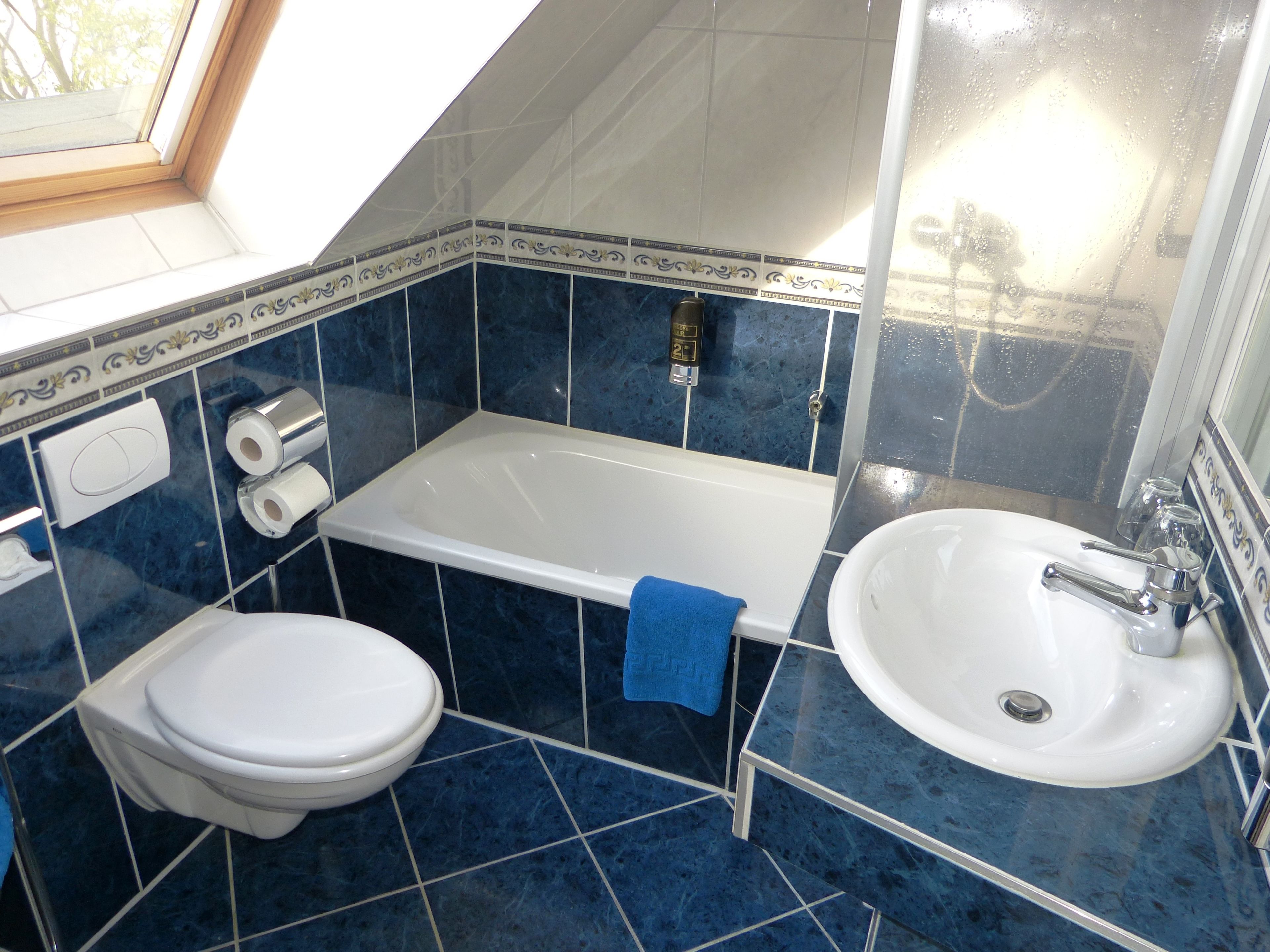 Ein Badezimmer mit Badewanne, Toilette und Waschbecken, alles mit blau gefliesten Wänden und Böden.