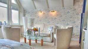 A cozy room with a glass coffee table, two armchairs, a sofa, and a patterned wallpaper. - Vogel Hotel Appartements & Spa (Rostock)