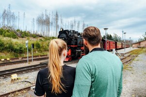 Una coppia in piedi vicino ai binari ferroviari, con un treno sullo sfondo.