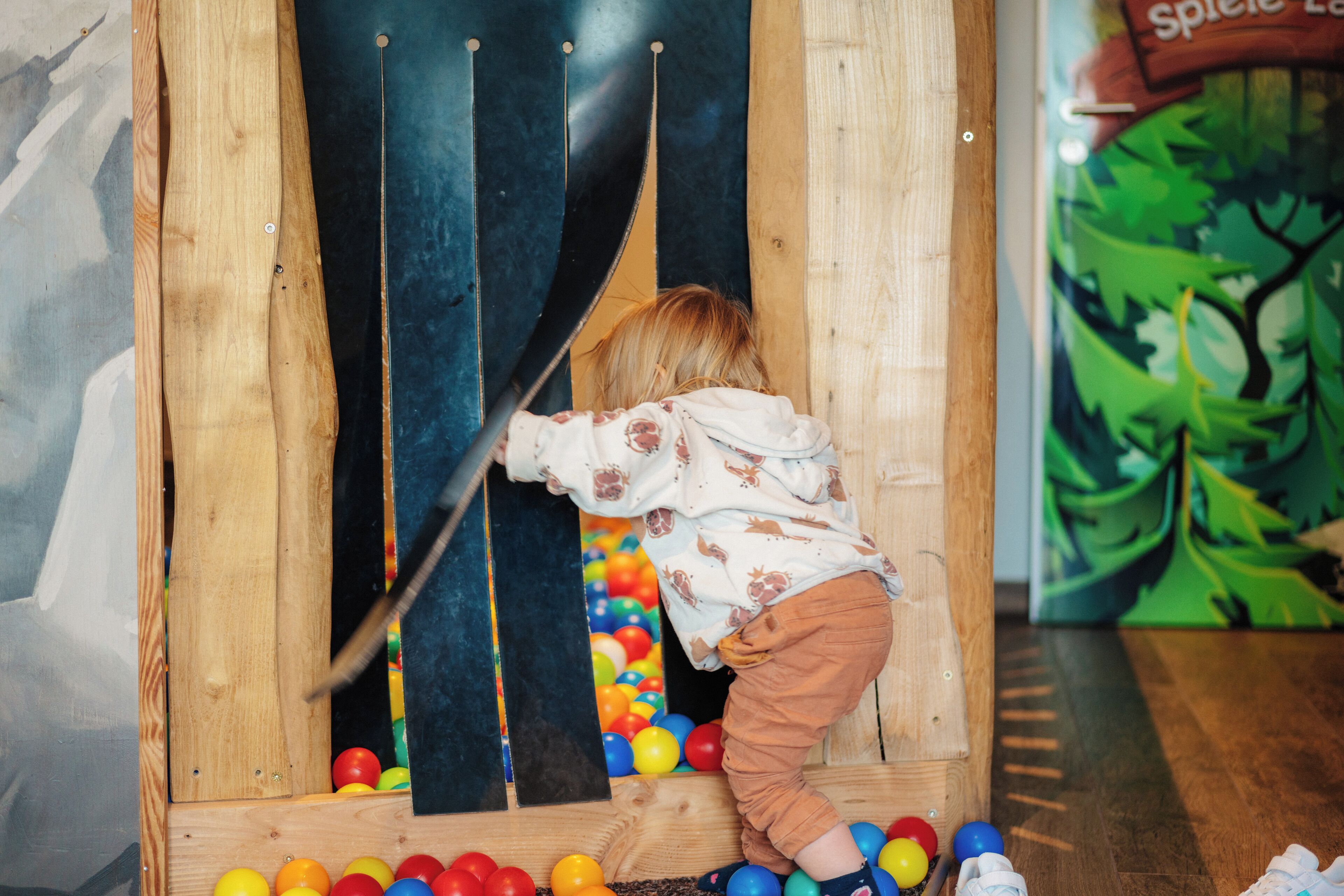 Un niño jugando con pelotas de colores en un área de juegos de madera.
