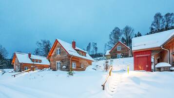 Eine Holzhütte mit schneebedecktem Dach, einer roten Tür und einem hölzernen Weg, der zum Eingang führt.